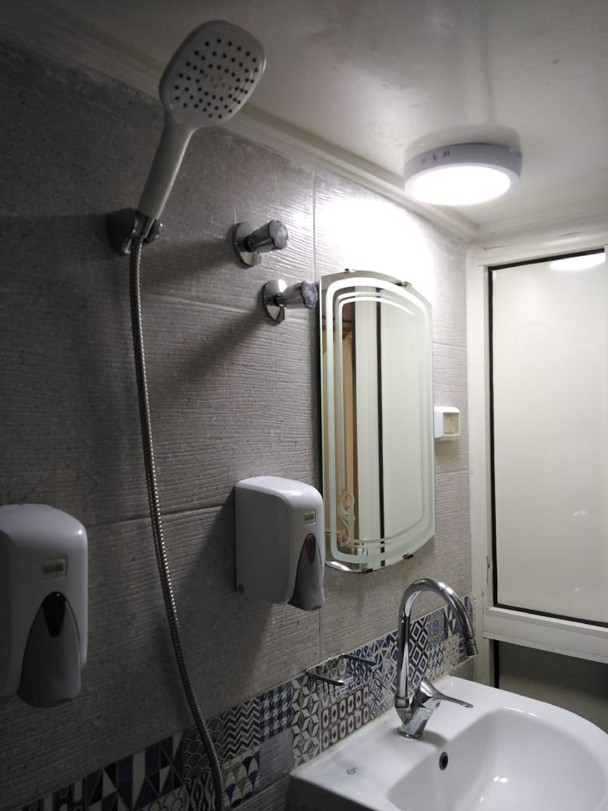 A bathroom with a shower, a sink, a mirror, and a soap dispenser.