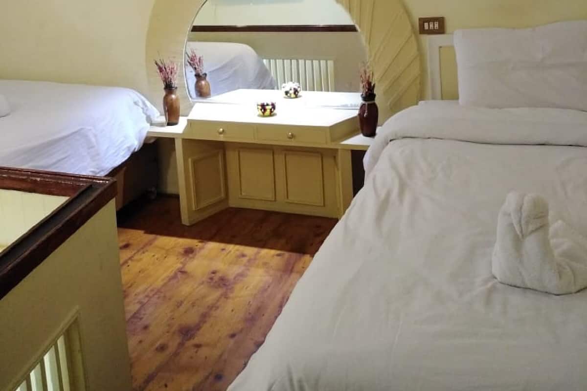 A hotel room with two beds, a small desk, and a mirror.