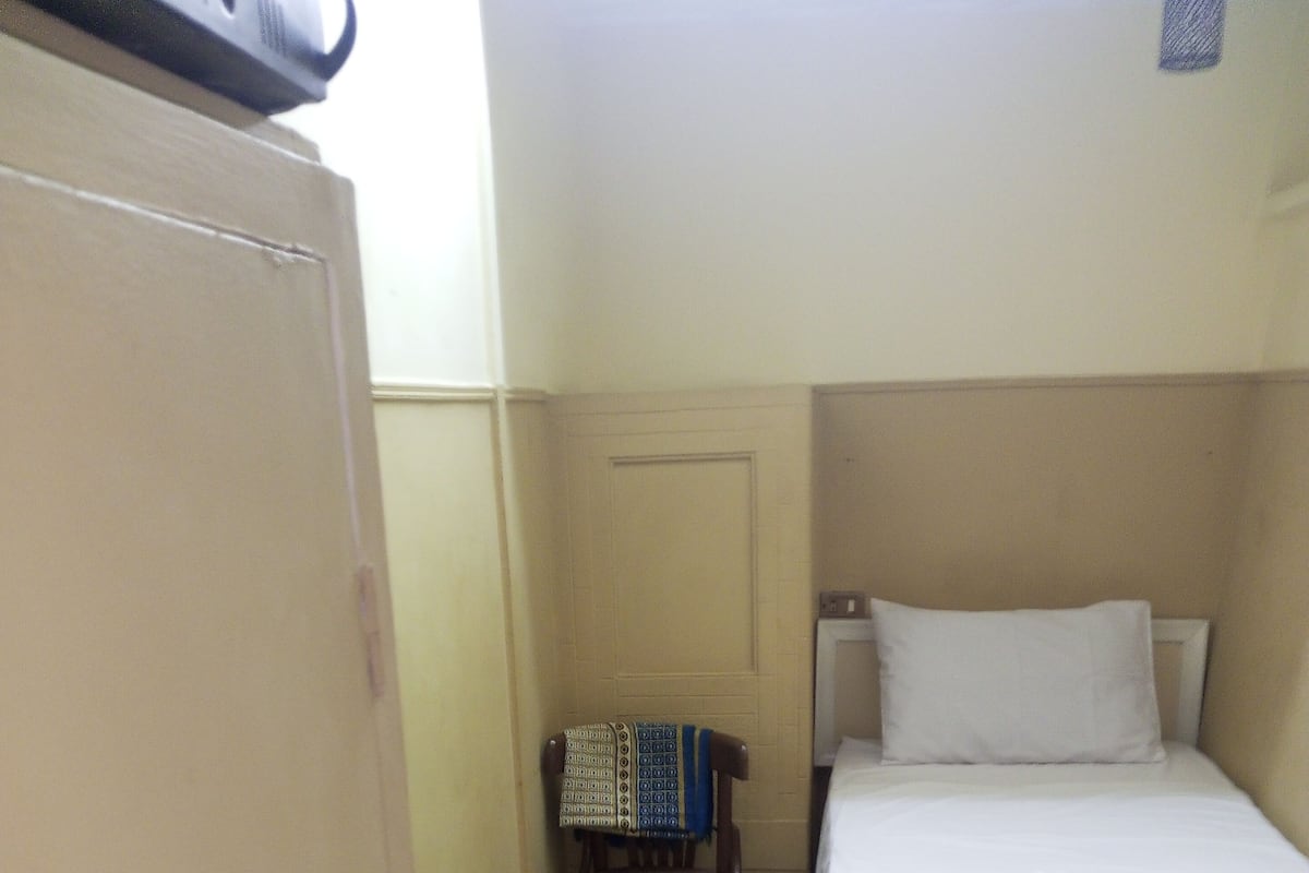 A small, neatly arranged hotel room with a single bed, a chair, and a wardrobe.
