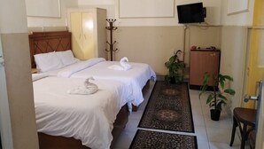 A hotel room with two beds, a TV, a coat rack, a desk, and a potted plant. - Panorama Palace hotel  (Cairo)