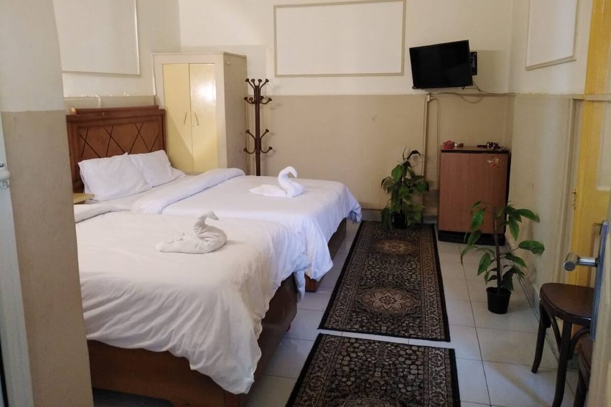 A hotel room with two beds, a TV, a coat rack, a desk, and a potted plant.