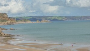 Un paysage côtier avec une plage, des affleurements rocheux et des collines à l’horizon.