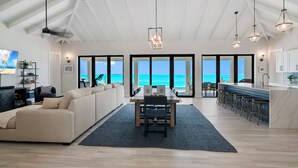 A spacious living area with a large sofa, a dining table, and a kitchen area with bar stools. - "New" 5 bedroom Exuma Beach Front Estate w/ Pool & No Neighbors on either side! (Harts)