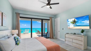 A bedroom with a bed, a ceiling fan, a TV, a sliding glass door leading to a balcony with a view of the ocean. - "New" 5 bedroom Exuma Beach Front Estate w/ Pool & No Neighbors on either side! (Harts)