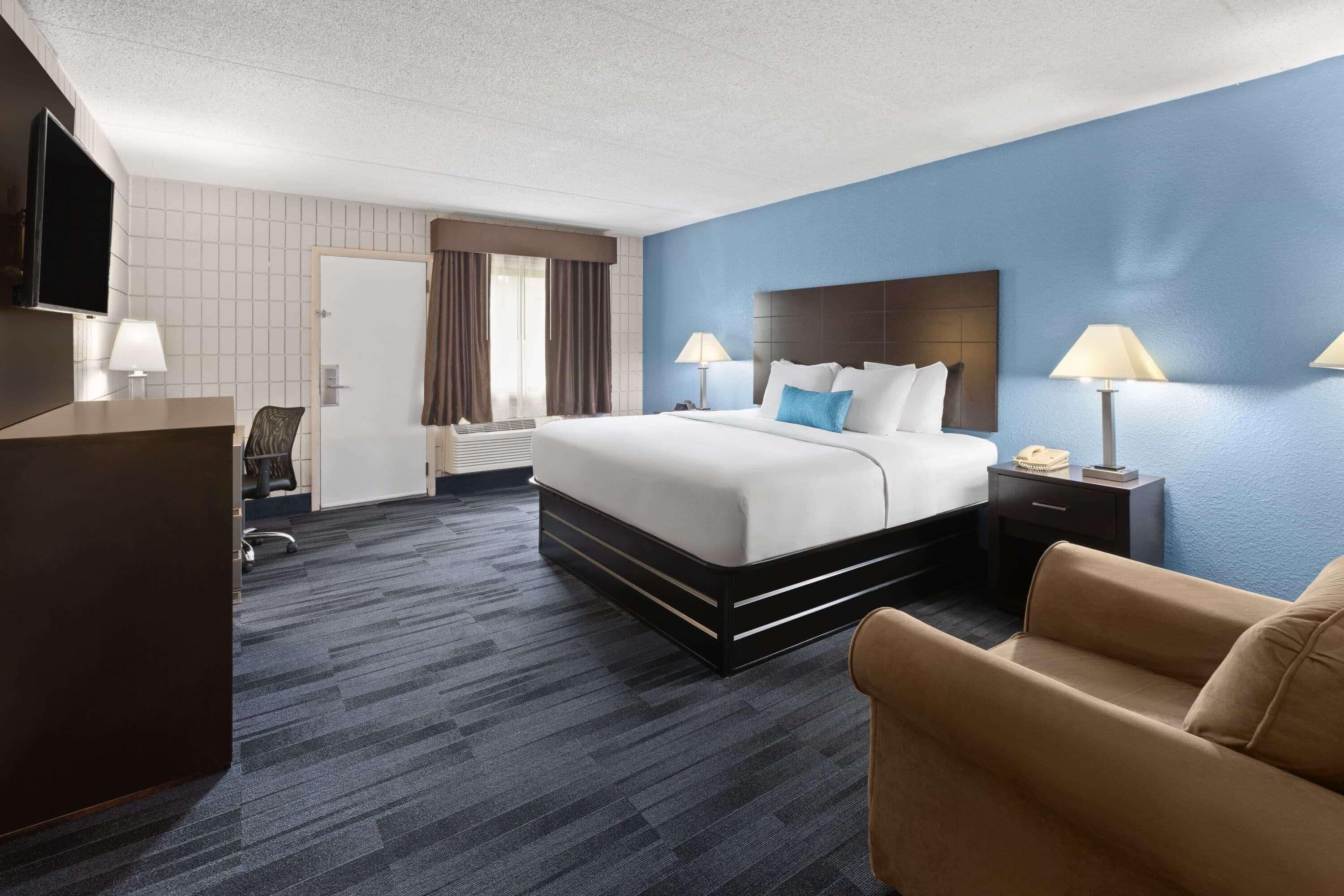 A hotel room with a bed, bedside tables, a desk, a TV, and a chair.