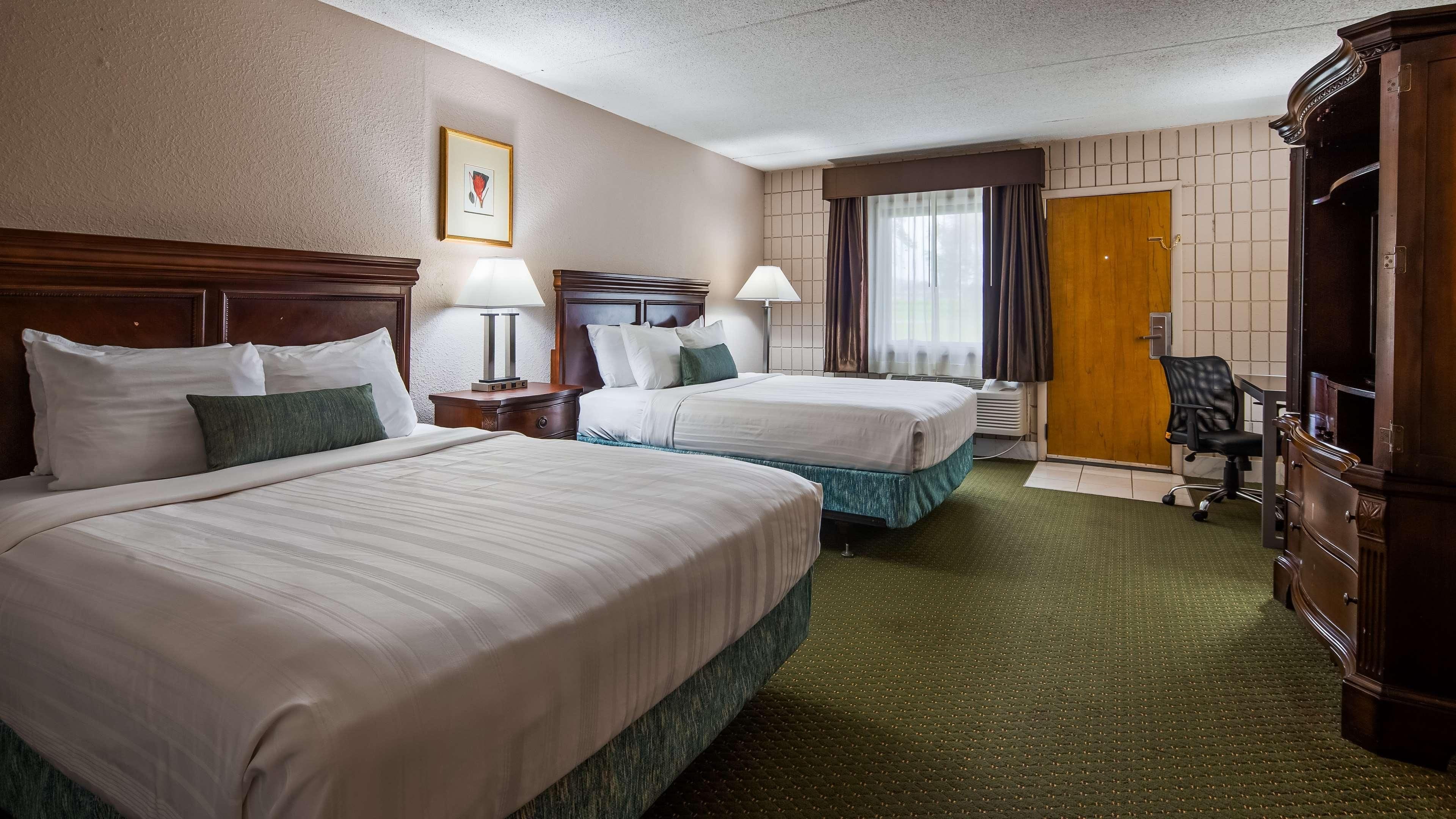 A hotel room with two beds, a desk, a chair, a wardrobe, and a window with curtains.