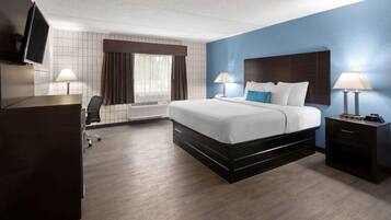A hotel room with a bed, bedside tables, a desk, a chair, a TV, and a window with curtains.