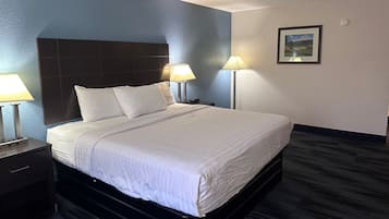 A hotel room with a bed, two bedside lamps, a nightstand, a framed picture on the wall, and a carpeted floor.