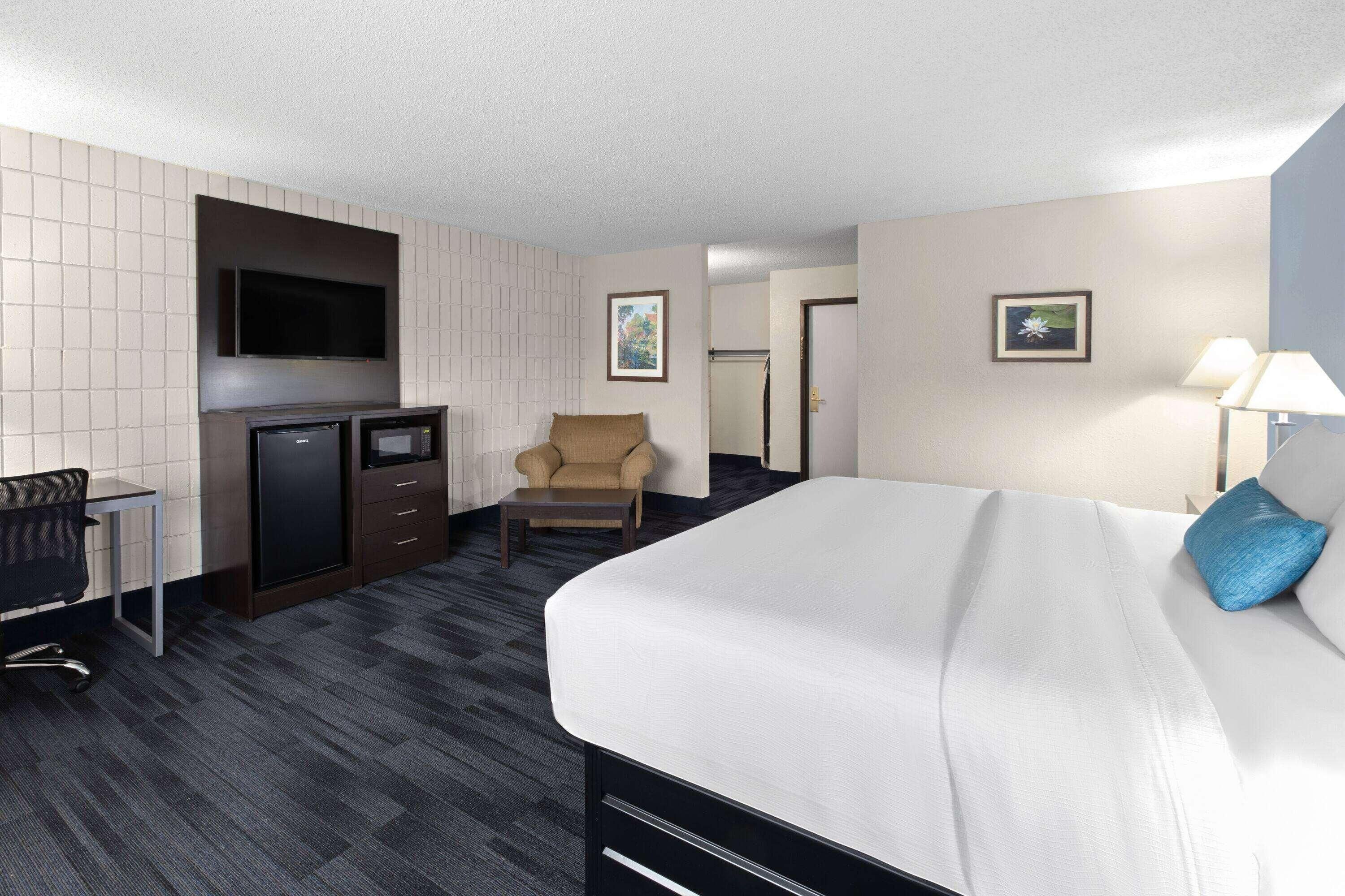 Habitación de hotel con cama, escritorio, silla, televisor y obras de arte en las paredes.