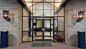 A hotel entrance with a glass door, a ramp, and two trash bins. - Baymont Inn And Suites By Wyndham Farmington Mo (Farmington)