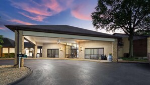 A hotel entrance with a covered driveway, a sign indicating the address, and a large tree to the right. - Baymont Inn And Suites By Wyndham Farmington Mo (Farmington)