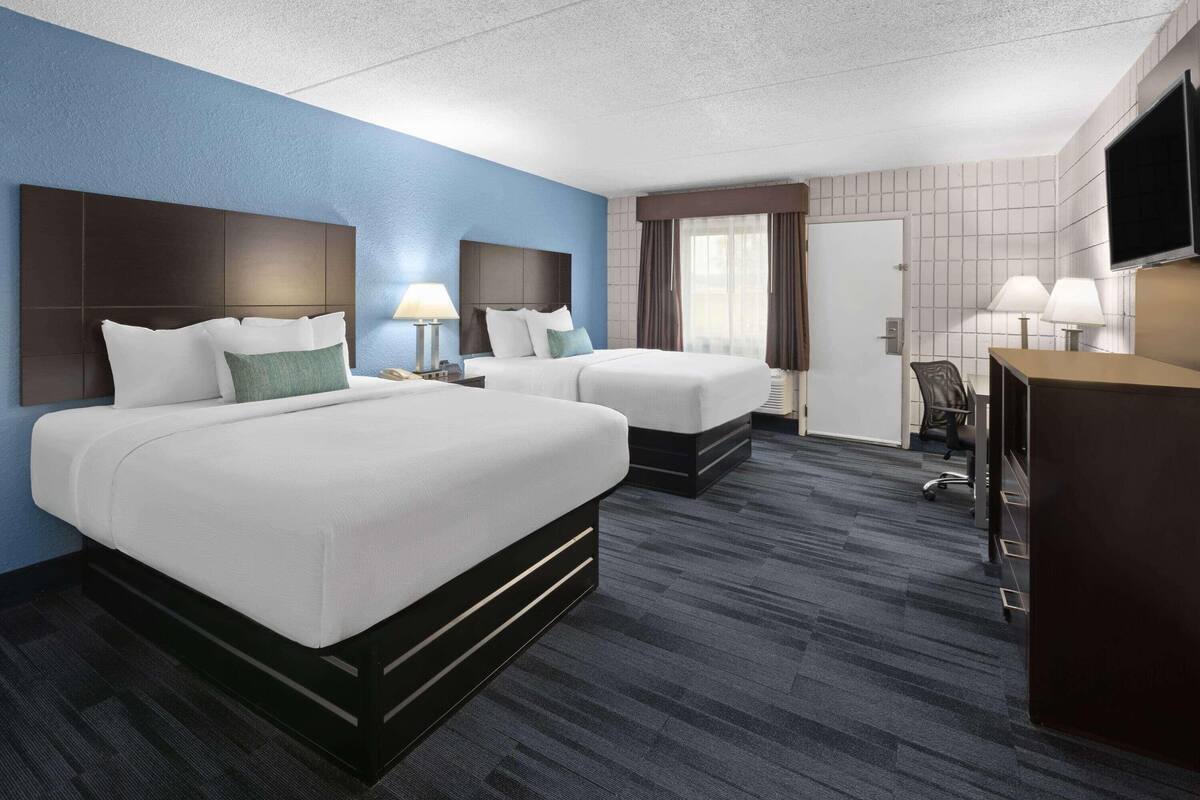 Een hotelkamer met twee bedden, een bureau, een stoel, een televisie en een raam met gordijnen.