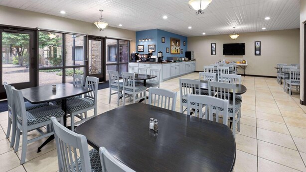 A dining area with tables and chairs, a kitchen area with appliances, and a television on the wall. - Baymont Inn And Suites By Wyndham Farmington Mo (Farmington)