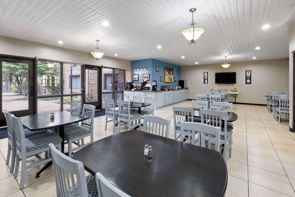 A dining area with tables and chairs, a kitchen area with appliances, and a television on the wall.