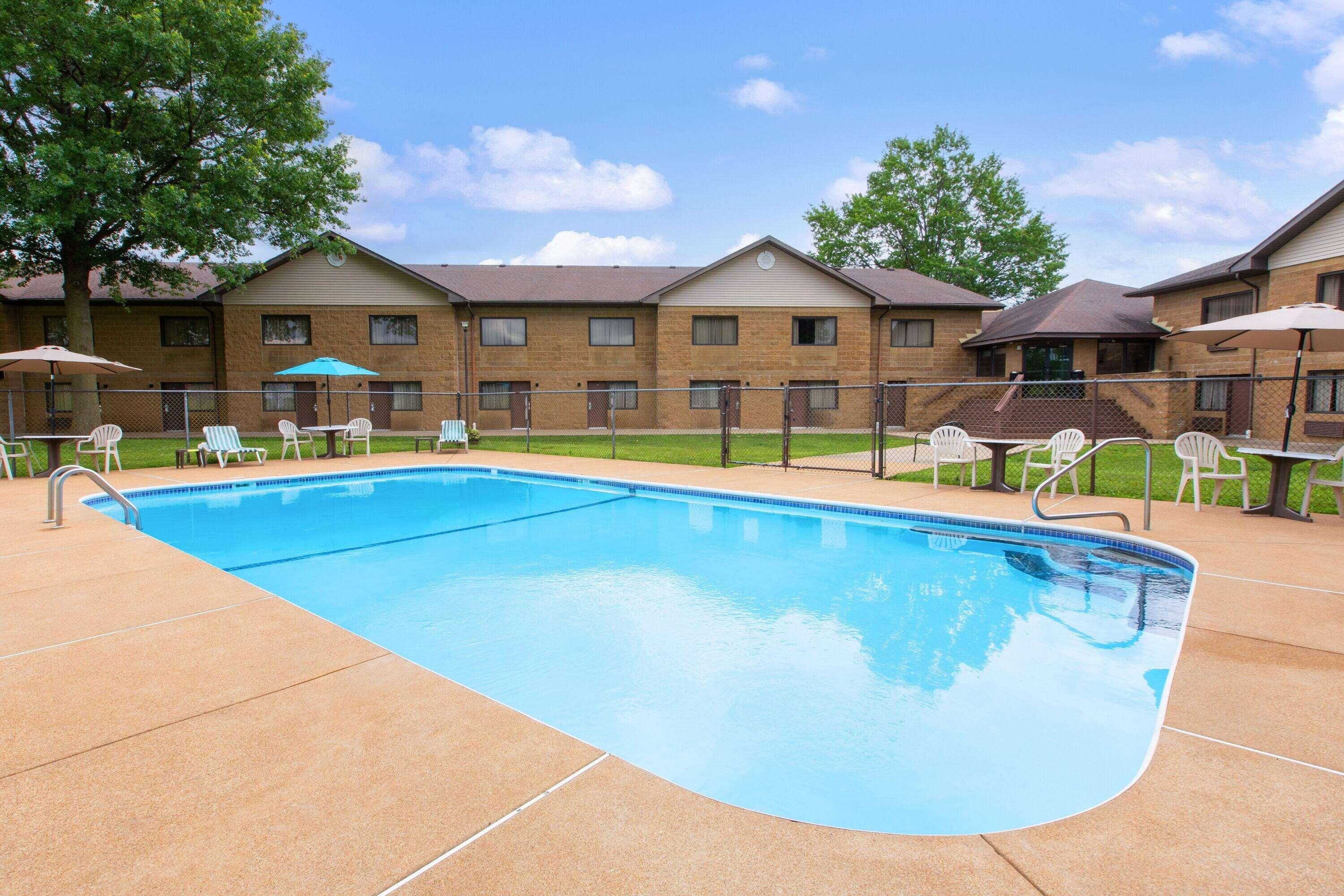 A swimming pool with lounge chairs and umbrellas, surrounded by brick buildings with windows and a clear sky.