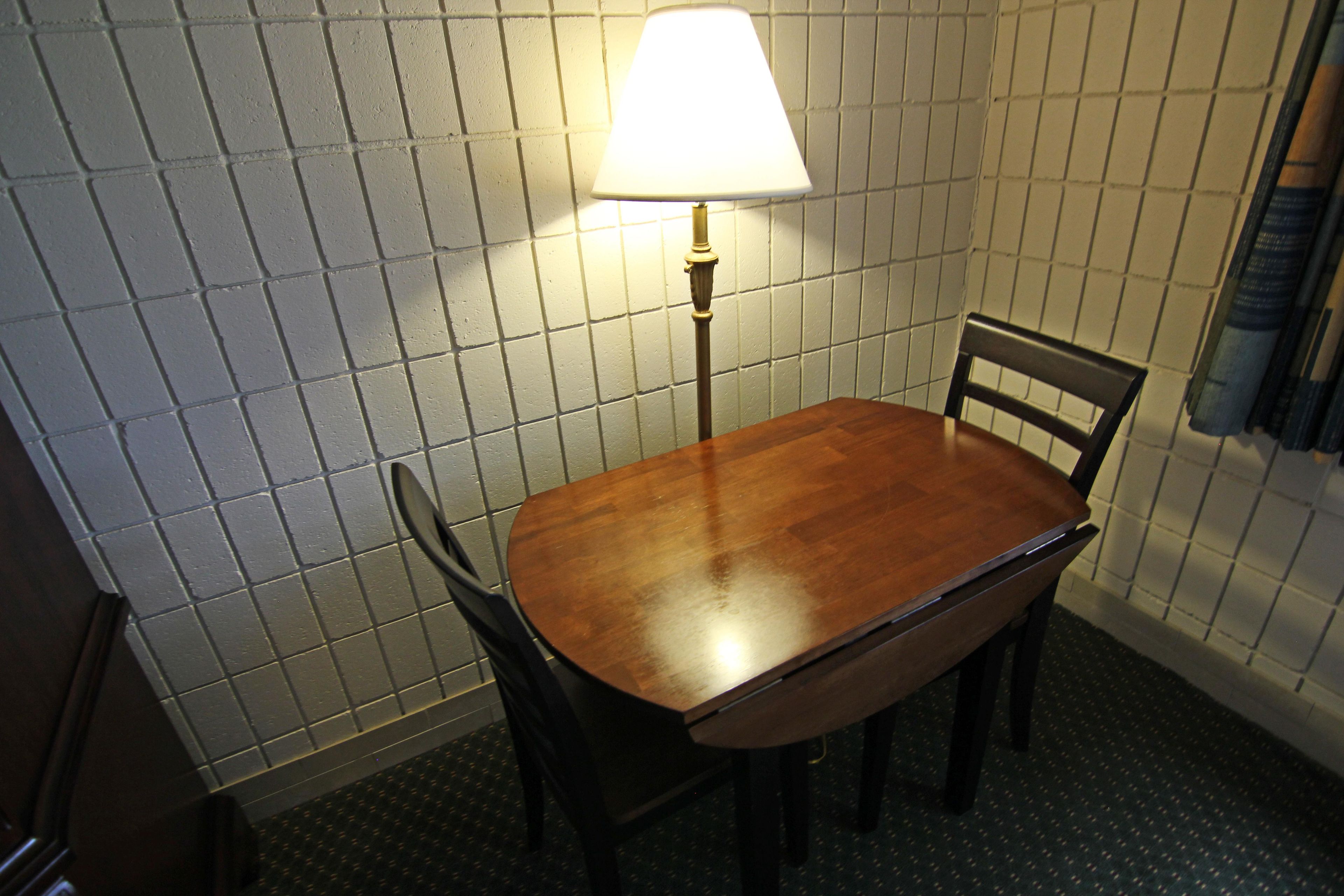 A small dining area with a table and chairs, a lamp, and a tiled wall.