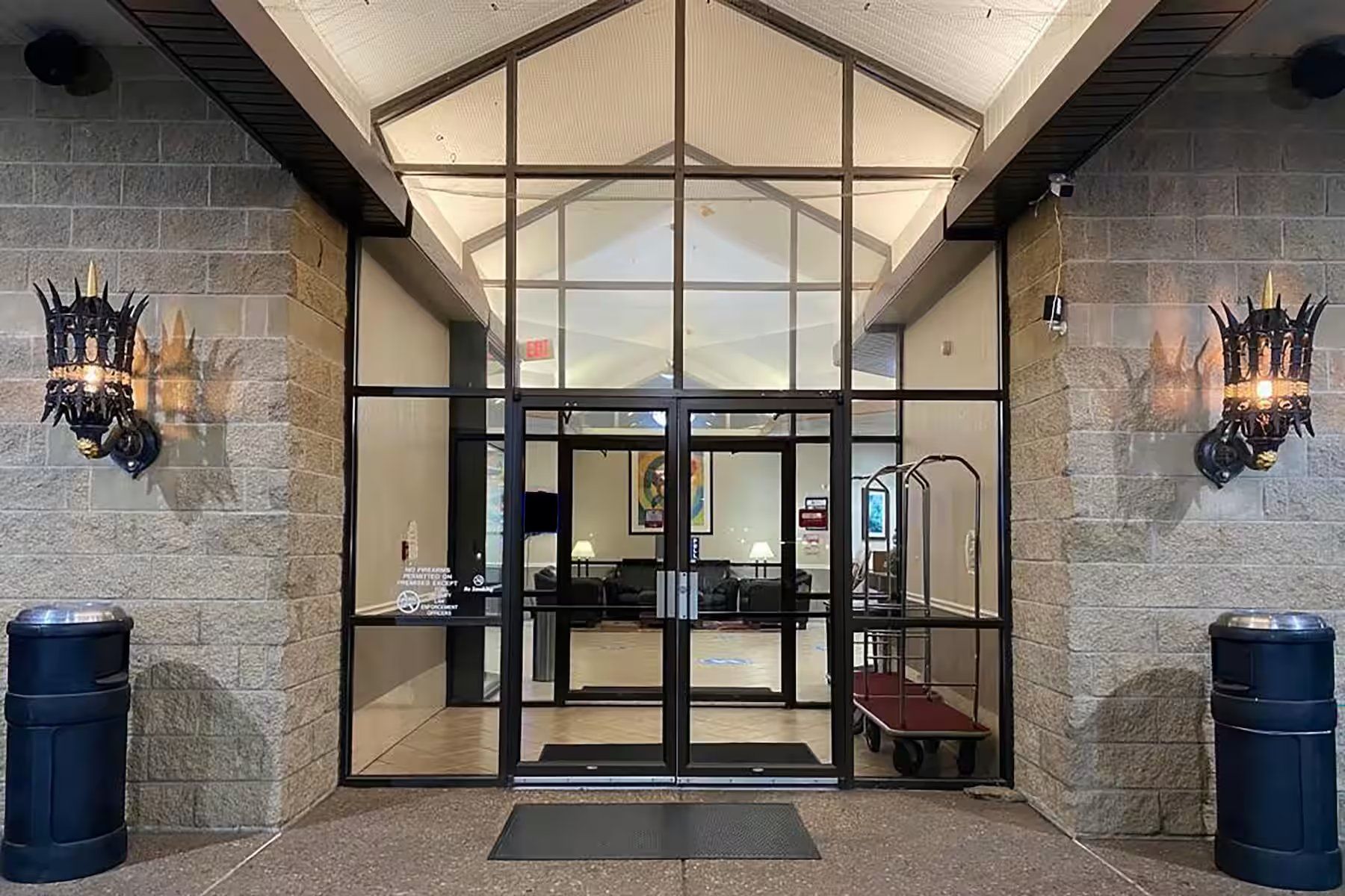 A hotel entrance with a glass door, a ramp, and two trash bins.