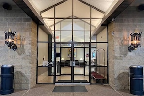 A hotel entrance with a glass door, a ramp, and two trash bins.