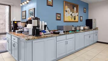 A kitchen with a granite countertop, coffee machines, and a large painting on the wall.