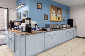 A kitchen with a granite countertop, coffee machines, and a large painting on the wall.