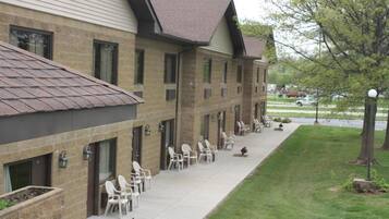 A hotel with a brick facade, multiple windows, outdoor seating area with chairs, and a well-maintained lawn.