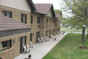 A hotel with a brick facade, multiple windows, outdoor seating area with chairs, and a well-maintained lawn.