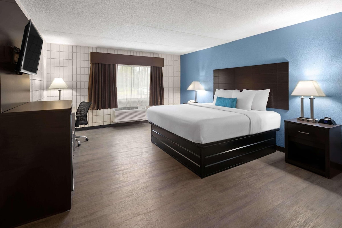 Een hotelkamer met een bed, nachtkastjes, een bureau, een stoel, een televisie en een raam met gordijnen.