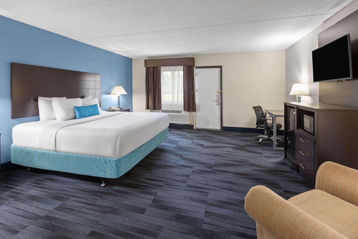 Een hotelkamer met een bed, bureau, stoel, televisie en een deur.