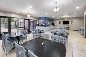 Un comedor con mesas y sillas, una cocina equipada y un televisor en la pared.