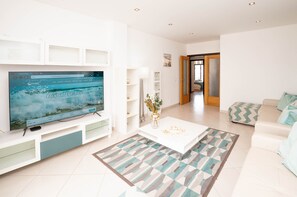 A modern living room with a flat-screen TV, a white coffee table, and a sofa.