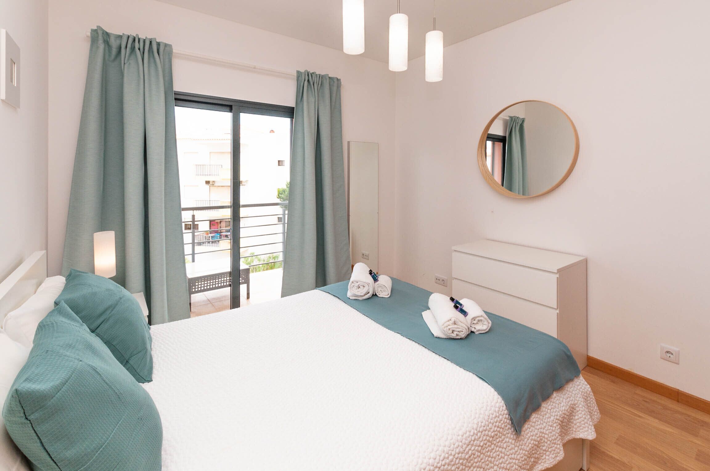 A bedroom with a bed, a dresser, a mirror, and a balcony view.