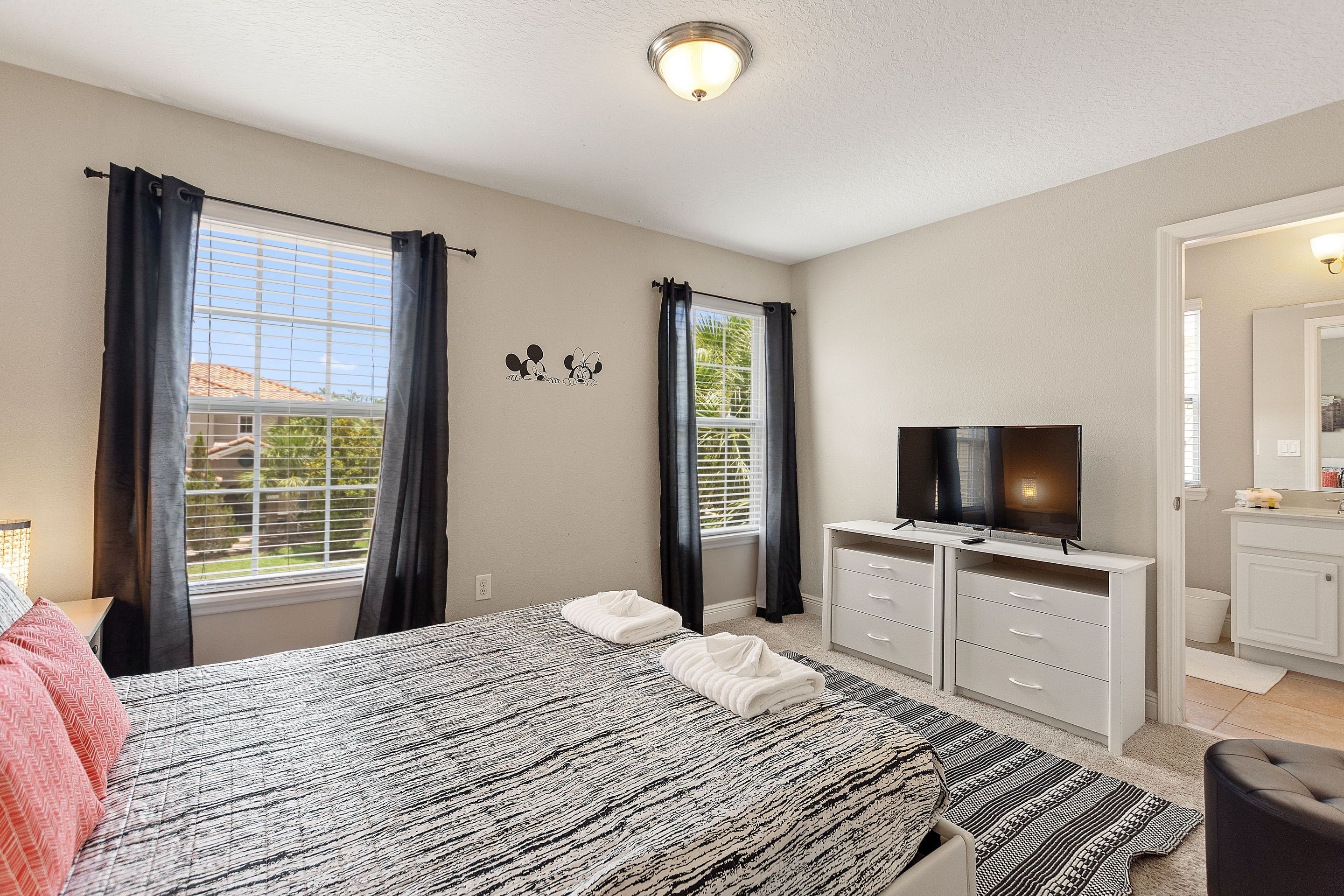 A bedroom with a bed, two bedside tables, a TV, and a window with curtains.
