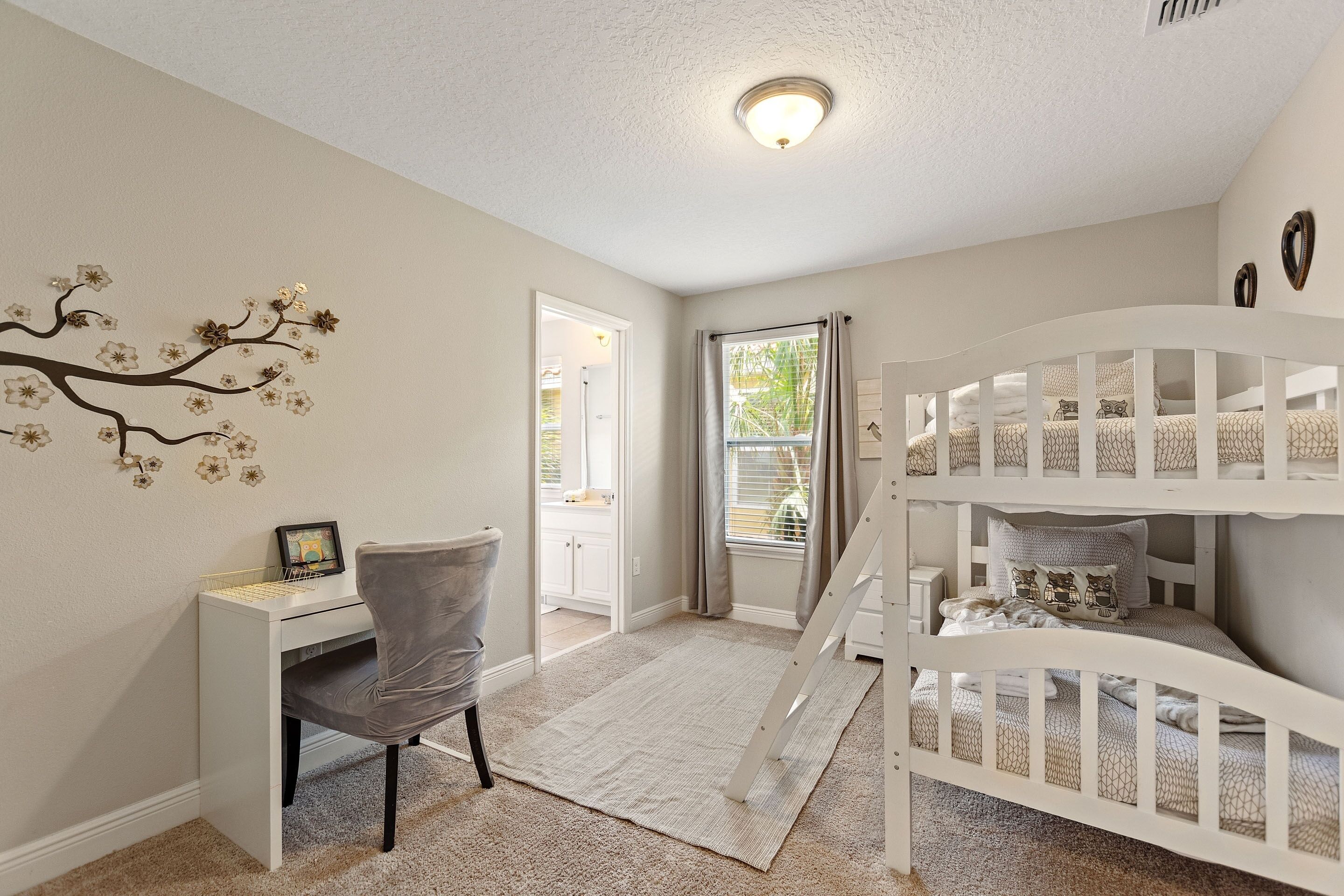 Une chambre d’enfant avec un lit superposé, un bureau, une chaise et un mur décoratif.