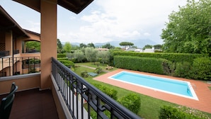 A balcony with a view of a swimming pool, neatly trimmed hedges, and distant mountains. - Casa della Rocca (Manerba del Garda)
