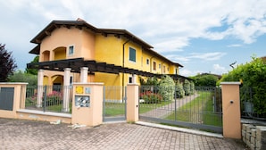 A yellow building with a gated entrance, a covered porch, and a well-maintained garden. - Casa della Rocca (Manerba del Garda)