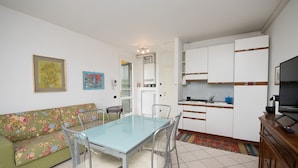 A modern kitchen with white cabinets, a dining table with chairs, and a sofa with floral upholstery. - Casa della Rocca (Manerba del Garda)