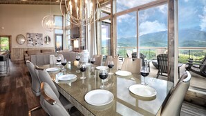 A dining area with a large table set for six, surrounded by chairs, with a view of mountains through large windows. - MIRACULOUS Luxury Cabin with Breathtaking Views! Theater, Hot Tub, Fire Pits (Gatlinburg)
