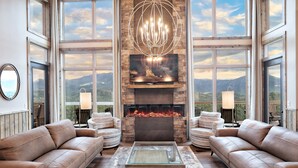 A spacious living room with leather sofas, a fireplace, and a large TV screen displaying a mountain view.