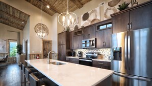 A modern kitchen with a large island, stainless steel appliances, and a wooden ceiling.