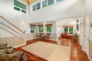 A spacious living area with a wooden floor, a dining table with chairs, a sofa, and a staircase with a railing.