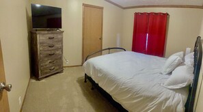 A bedroom with a bed, a dresser, a television, and a door. - Wyoming Prairie Place (Gillette)
