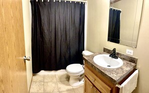 A bathroom with a toilet, sink, and shower curtain. - Wyoming Prairie Place (Gillette)