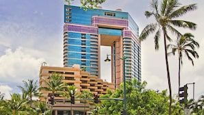 A multi-story hotel with a distinctive blue and purple facade, surrounded by palm trees and a clear sky.