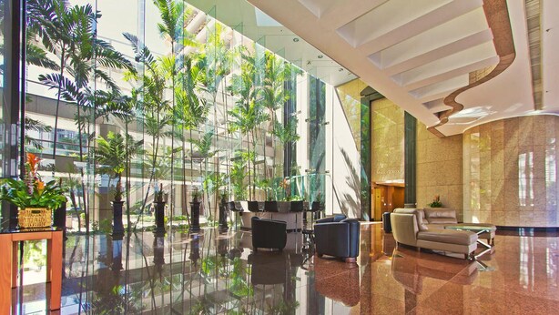 A spacious lobby with a glass wall, modern furniture, and indoor plants.