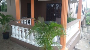 Un espacio al aire libre cubierto con una mesa y sillas, rodeado de plantas en macetas y columnas anaranjadas.