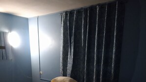Una cama individual con un colchón blanco y dos almohadas, una pared azul oscuro y una ventana con cortinas.