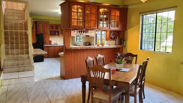 Una cocina amplia con armarios de madera, un comedor con mesa y sillas, y una escalera que sube a otro nivel.