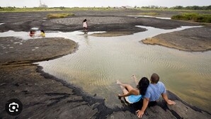 Paisaje natural con un cuerpo de agua embarrado y personas realizando actividades acuáticas.
