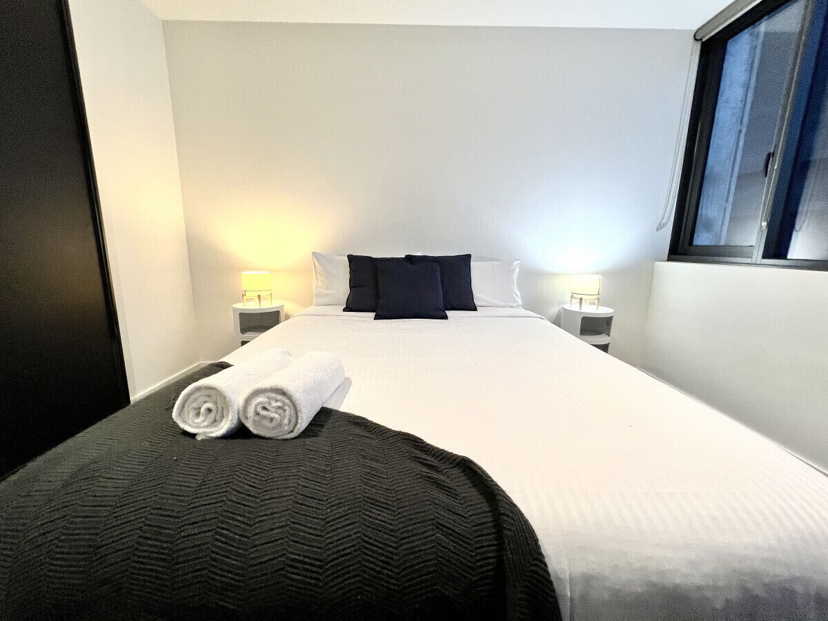 Een hotelkamer met een netjes opgemaakt bed, twee bedlampen en een raam met uitzicht.