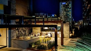 An outdoor dining area with tables and chairs, surrounded by greenery and a stone pathway. - 2 BR in High-Rise Building at Manhattan (Melbourne)